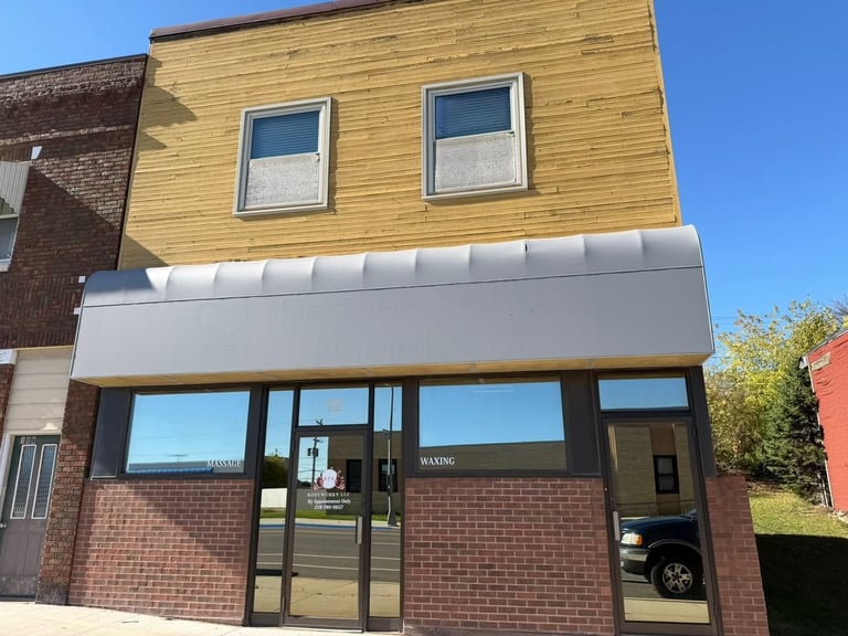 Modern storefront with brick base and yellow wood upper level, featuring large windows and white awning against clear blue sky
