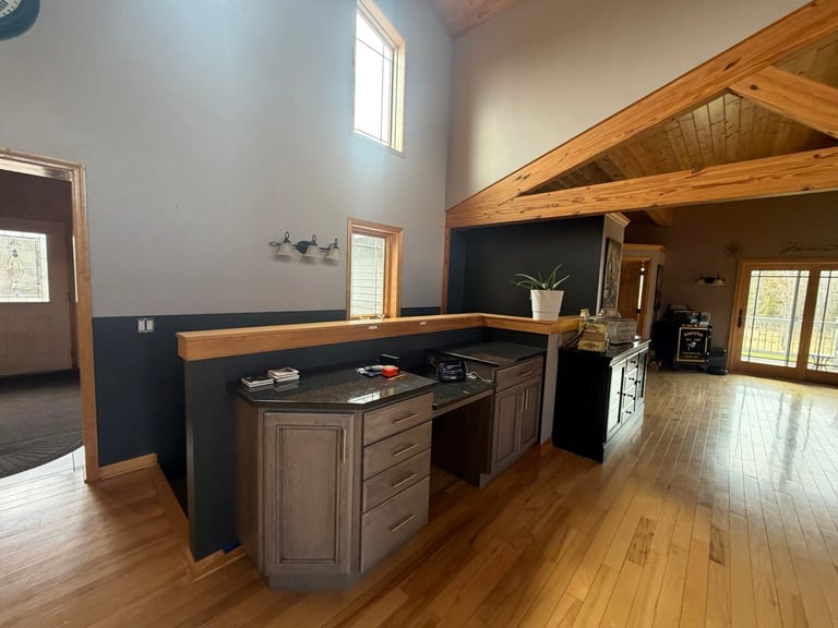 Modern kitchen with wooden beams, island, dark blue lower walls, and hardwood flooring in open-concept space.