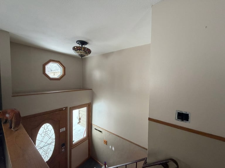 Interior entryway with wooden door, oval window, wall clock, and two-tone cream and wood-paneled walls