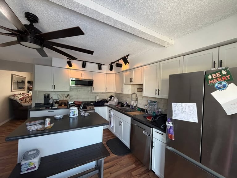 Modern kitchen with white cabinetry, black countertops, stainless steel appliances, and dark wood flooring
