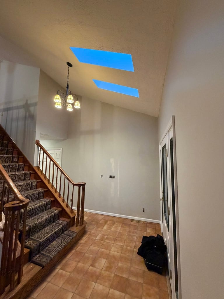 Bright entryway with wooden staircase, pendant lights, and two large blue skylights on angled ceiling