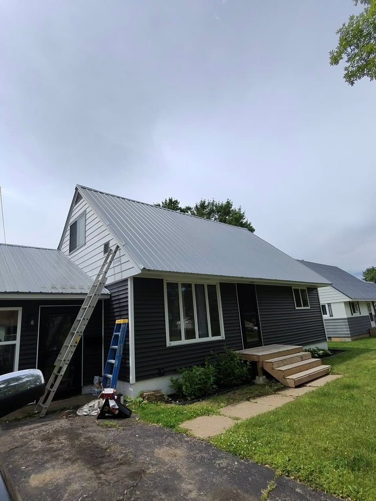 Modern farmhouse with metal roof, black siding, and white trim under construction with ladder and wooden deck steps