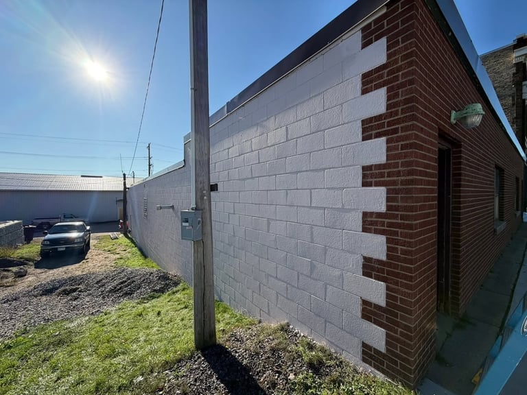 Modern industrial building with mixed concrete and brown brick exterior, sunny clear day with grassy lawn and parked car visible.
