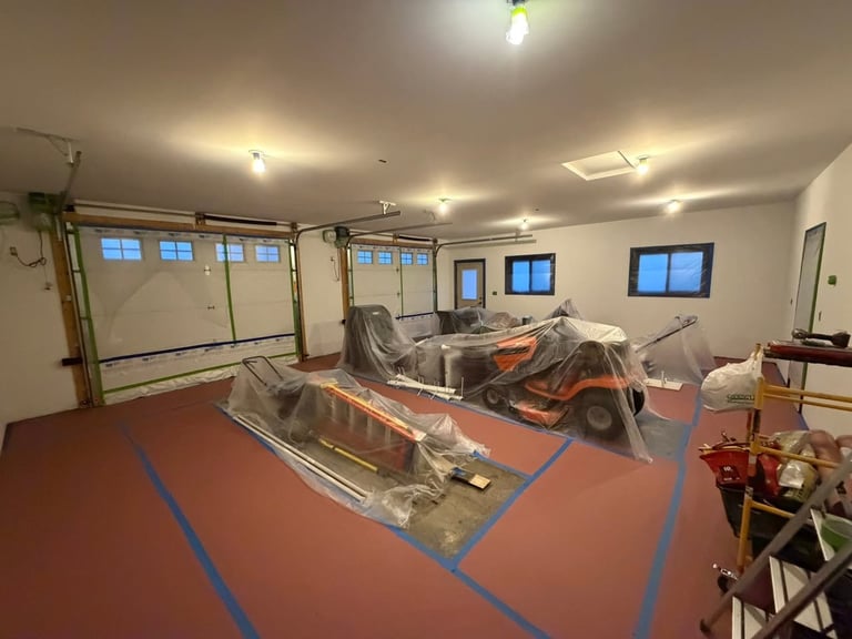 Indoor garage workshop with vehicles covered in plastic sheeting on a red floor with blue line markings