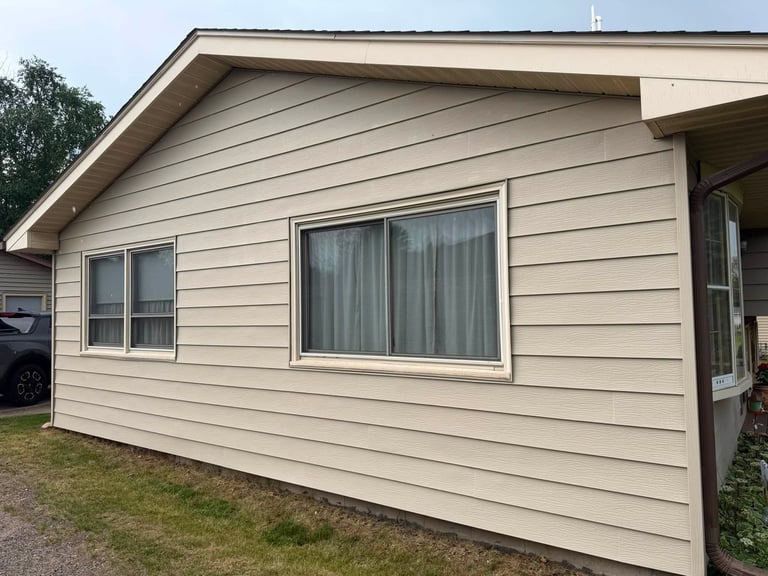 Single-story house with beige vinyl siding, multiple windows, and green lawn in front