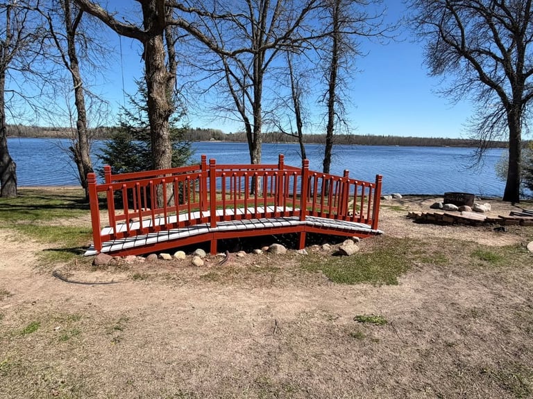 Red wooden bridge over a sandy area near a lake with bare trees and blue sky