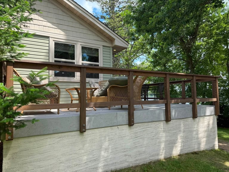 A residential house with a wooden pergola deck structure and white railings, surrounded by green trees and landscaping.