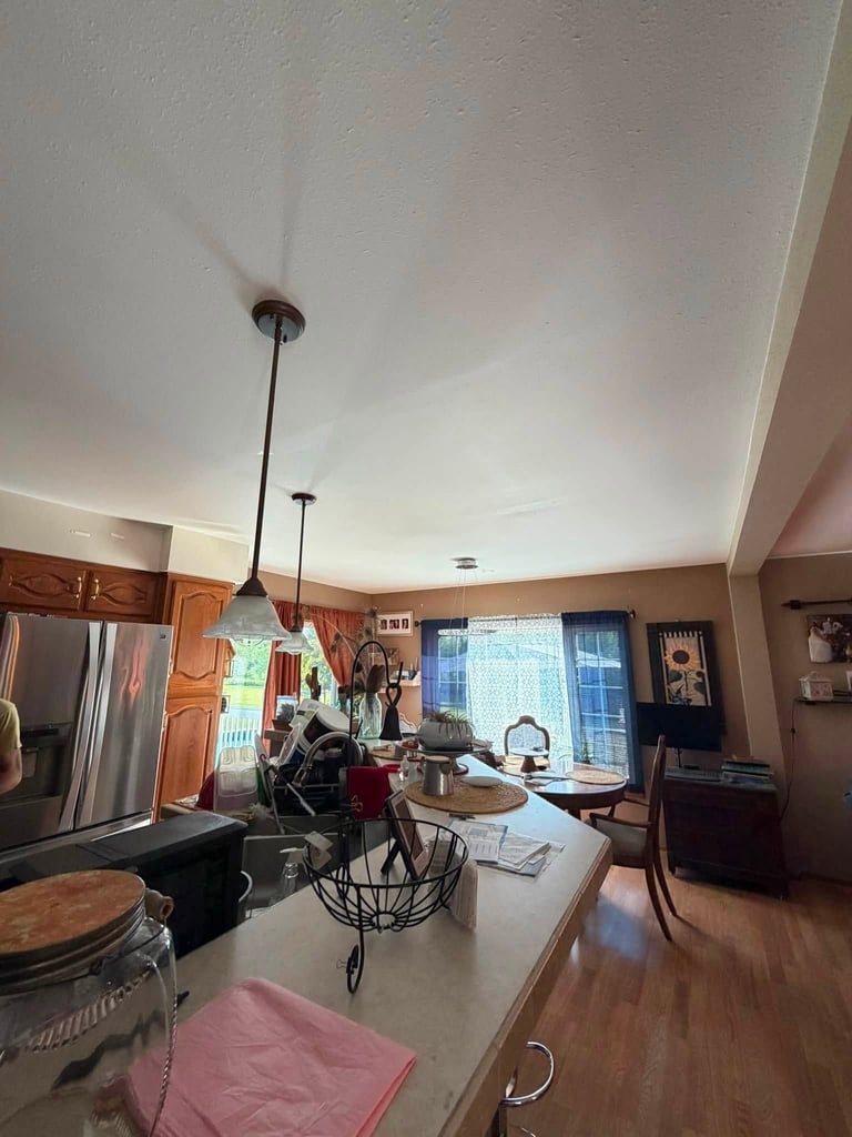 Modern kitchen interior with white ceiling, pendant lights, stainless steel appliances, and wooden flooring with countertop island