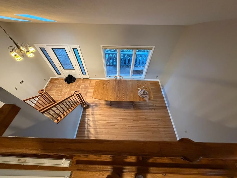 Modern loft interior with wooden flooring, skylight windows, pendant lighting, and wooden railings viewed from above